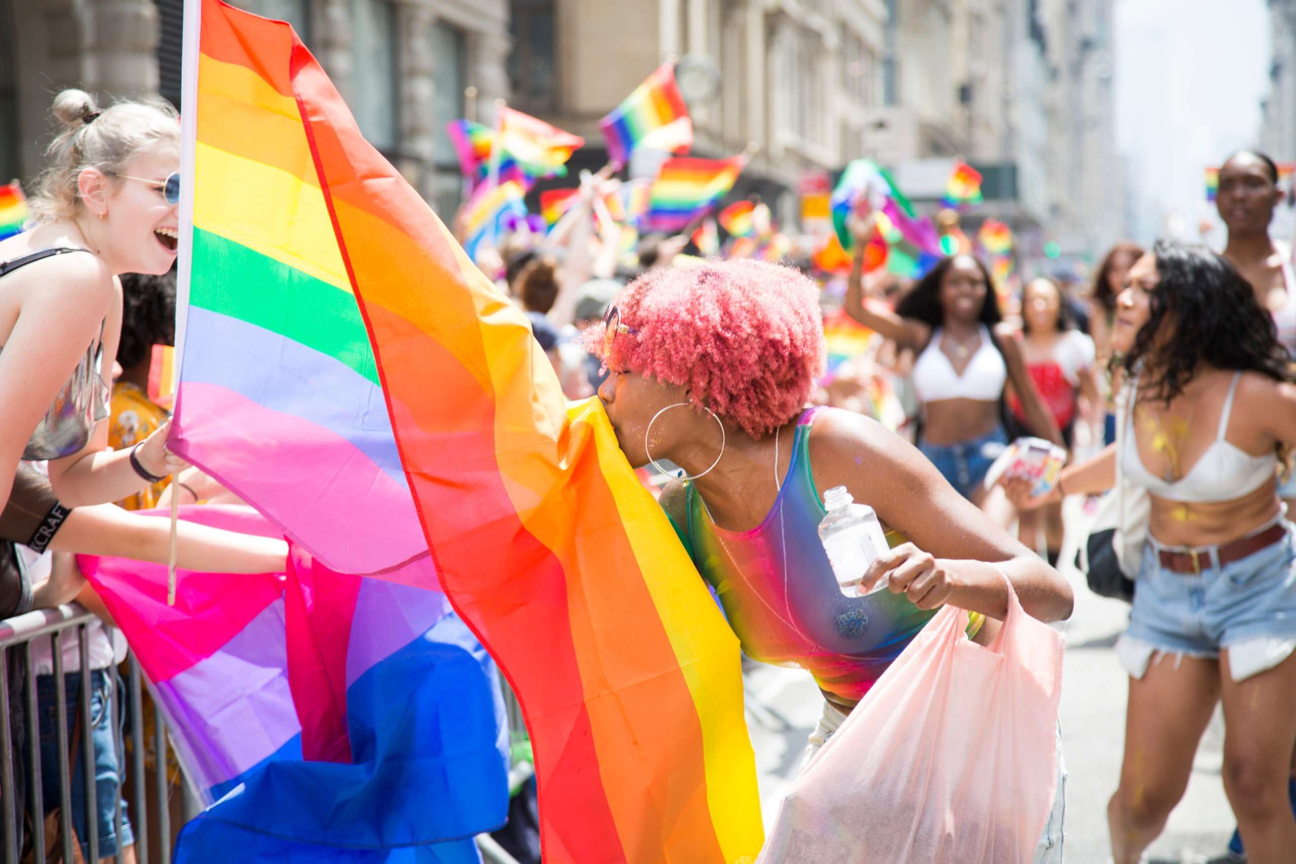 A woman with pink hair gives a kiss to someone behind a rainbow colored flag during the Pride Parade in NYC