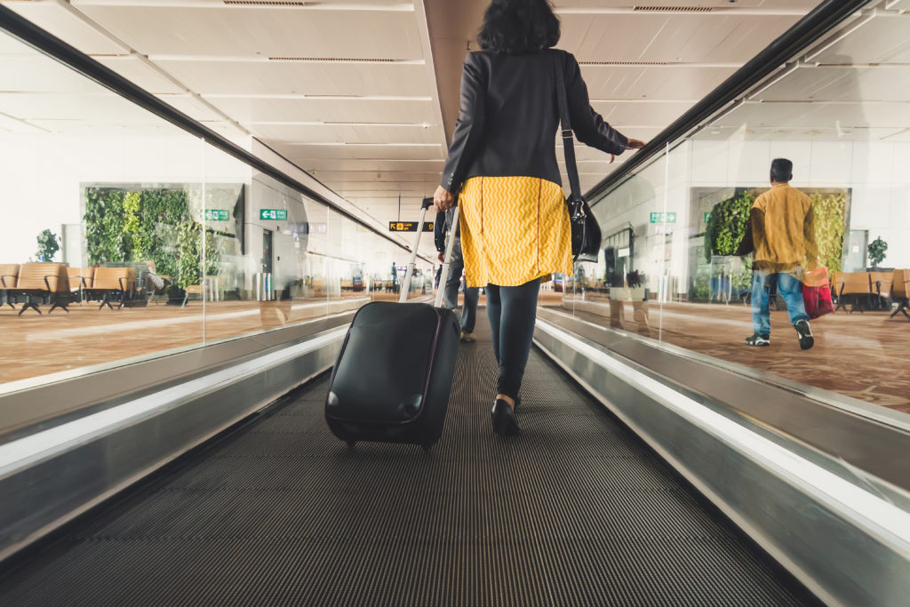Where to Live Near Airports for Travelers - Young girl traveler walking with carrying hold suitcase in the airport. Tourist Concept. escalator, interior of airport.
