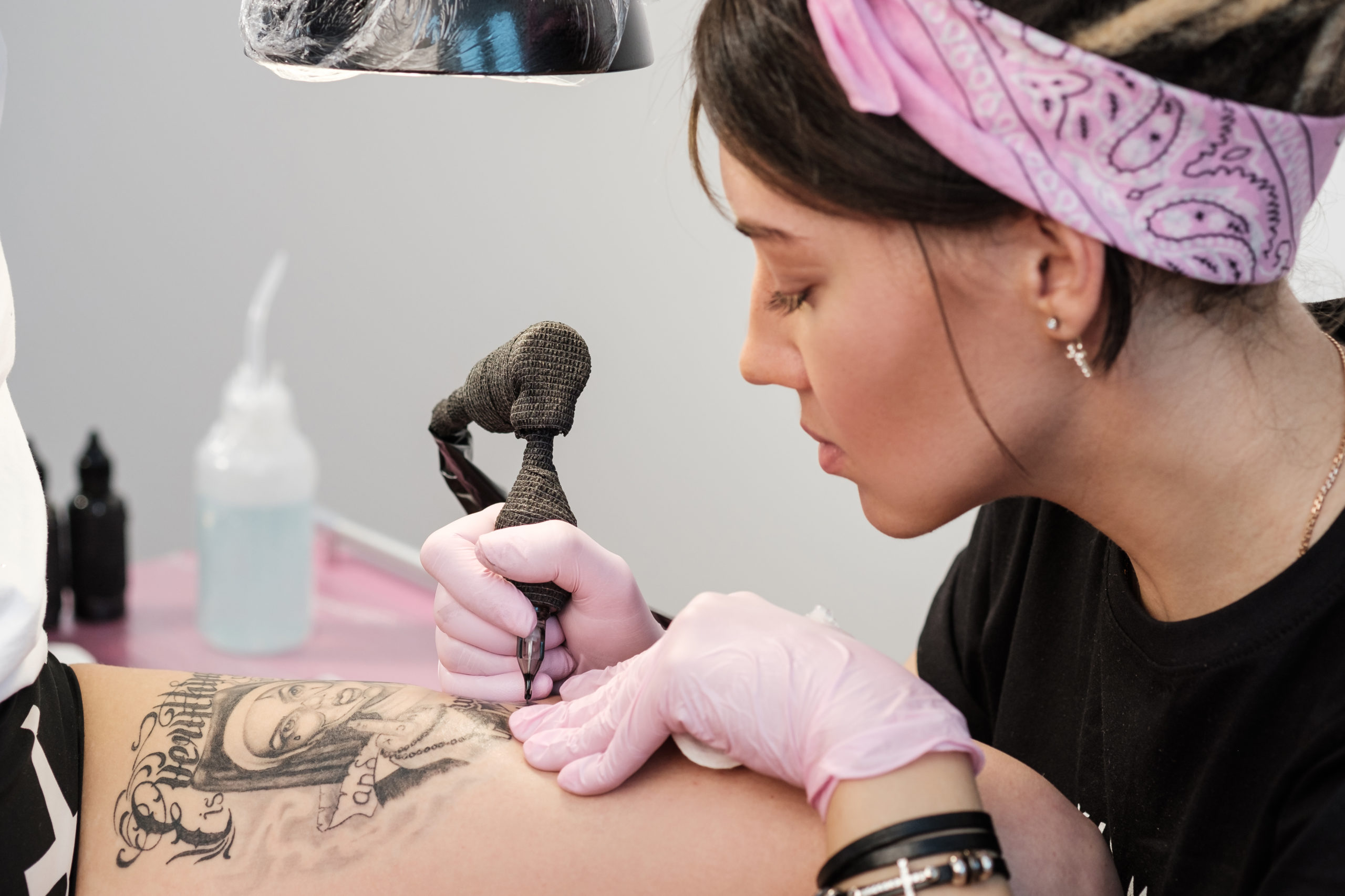 4 Very Popular Tattoo and Piercing Parlors in NYC - Female Tattoo artist wearing a pink headband and gloves giving a thigh tattoo