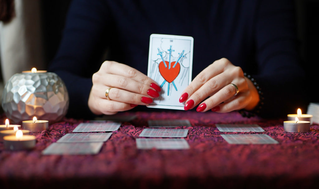 3 Popular Psychics in NYC: Tarot reader picking tarot cards on table near burning candlelight in dark